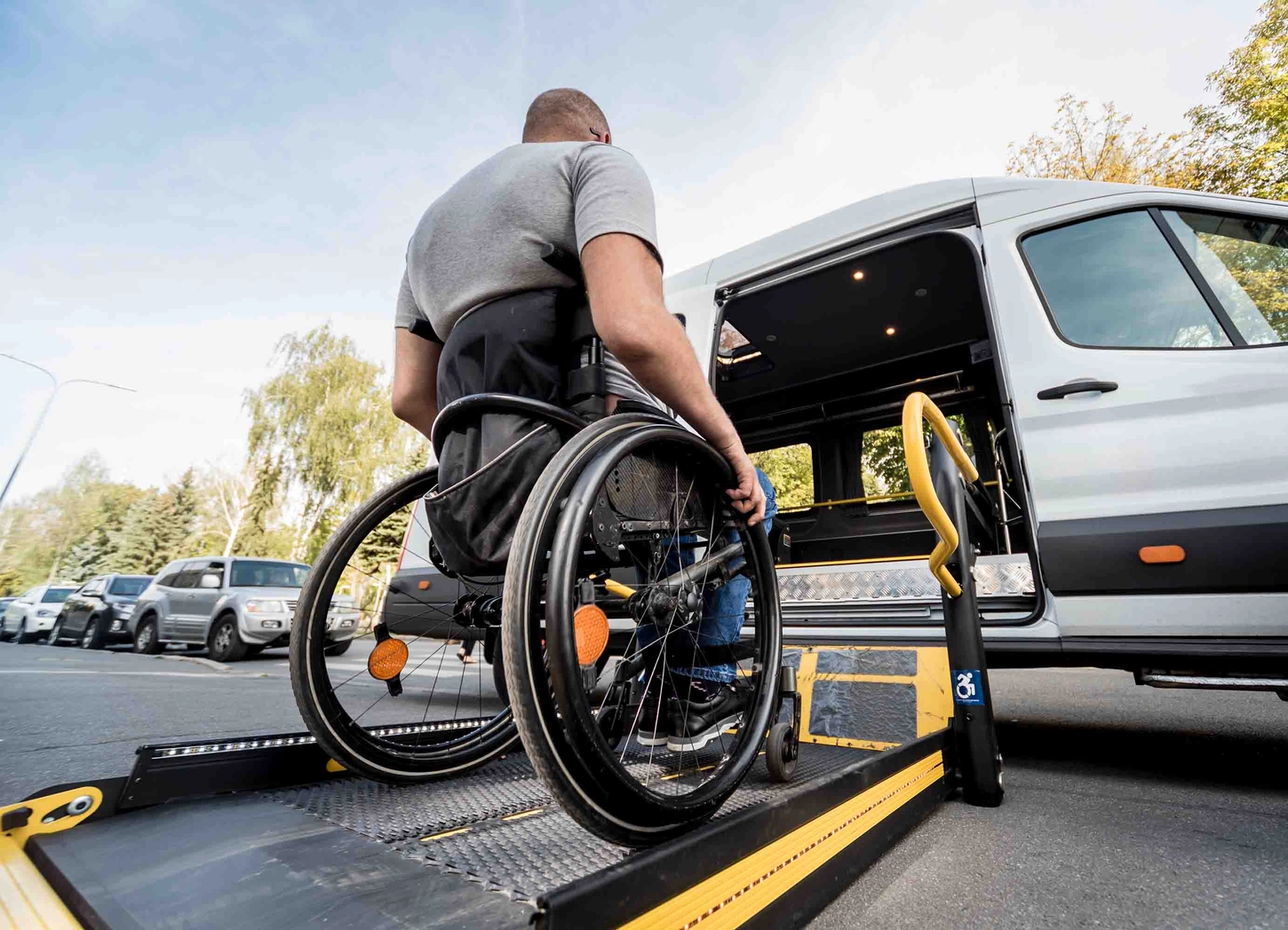 Handicap Fahrzeuge GmbH - Ein Mann im Rollstuhl fährt zum Lift eines Spezialfahrzeugs.